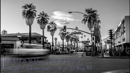 Long exposure image of car driving down Palm Canyon in Palm Springs past the palm trees along the road side.
